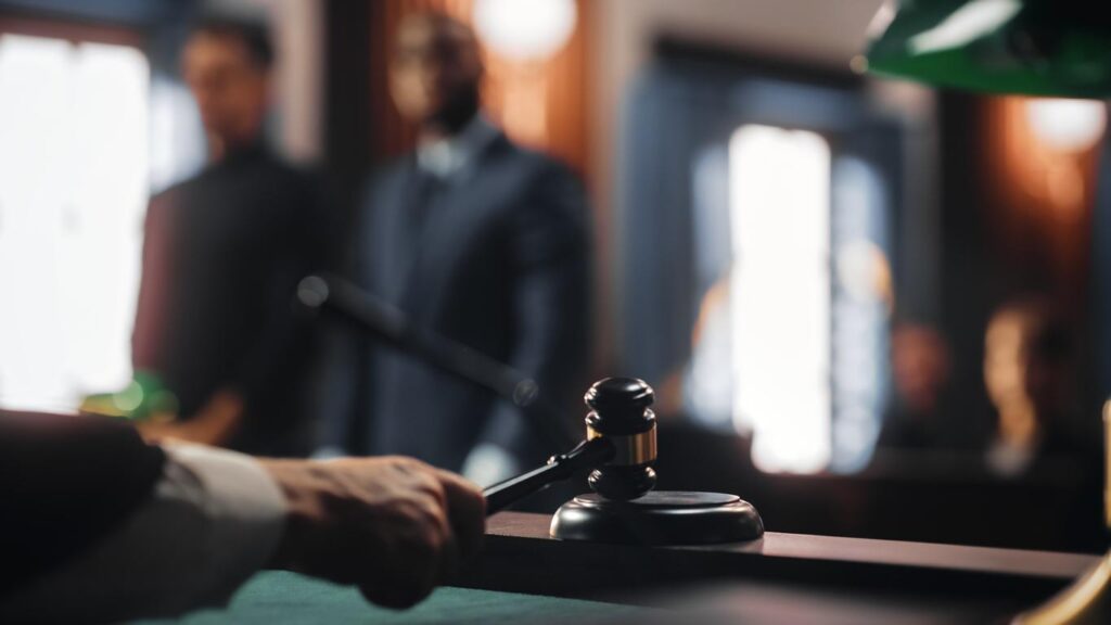 Two people in court stand blurred in background with judge's hand on gavel in forefront of photo.