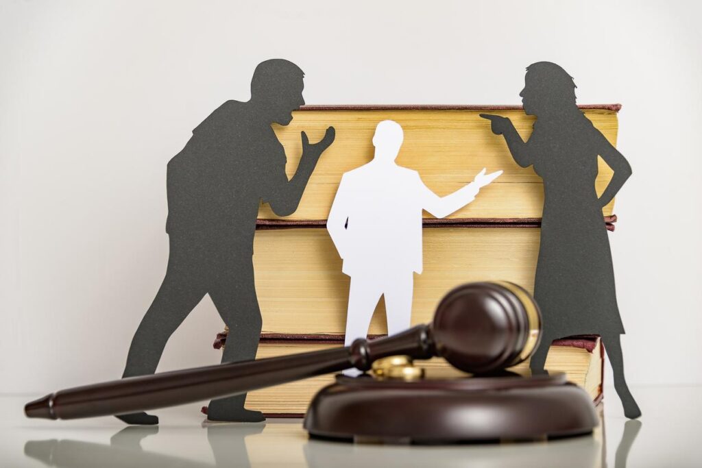 Paper silhouettes of people arguing with gavel resting in forefront of photo.